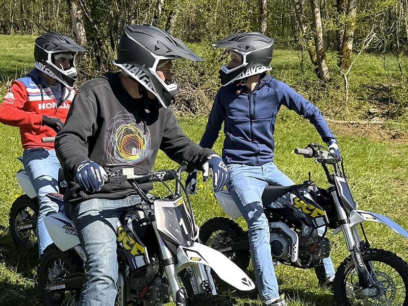Gros plan sur trois jeunes à moto discutant ensemble, tous casqués et habillés de façon décontractée.