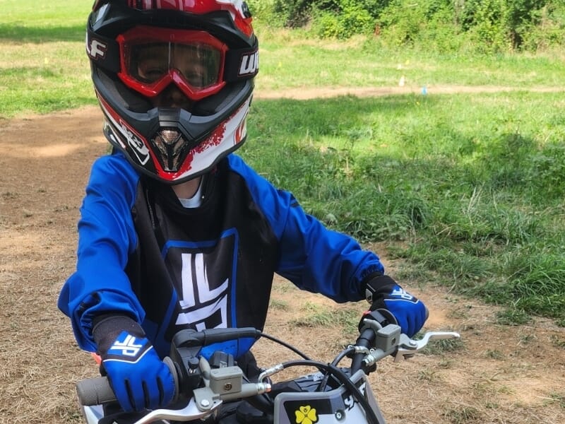 Enfant en tenue de moto bleue et casque rouge noir, prêt à piloter lors d'un stage motocross enfant près de Lons-le-Saunier.