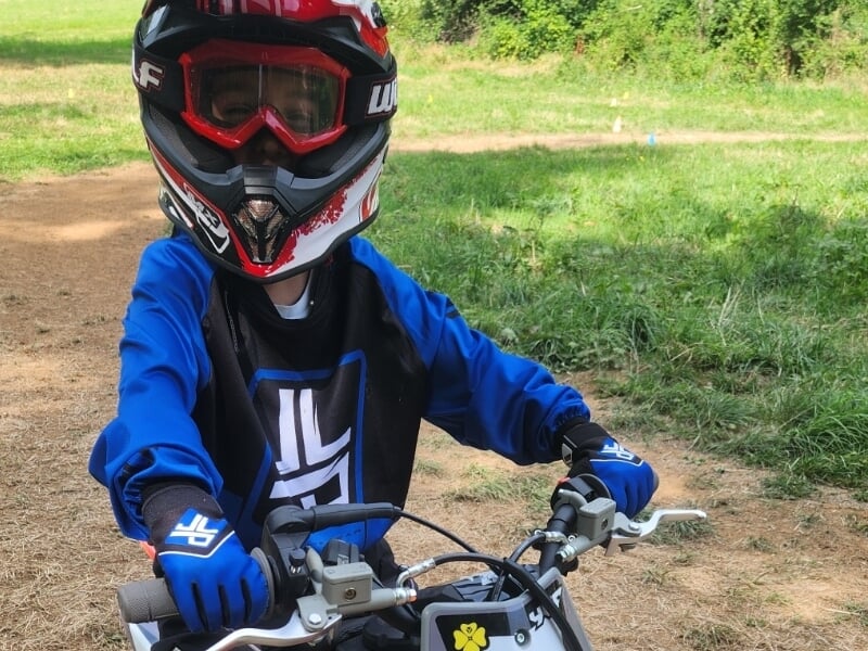Enfant en tenue de moto bleue et casque rouge noir, prêt à piloter lors d'un stage motocross enfant près de Lons-le-Saunier.