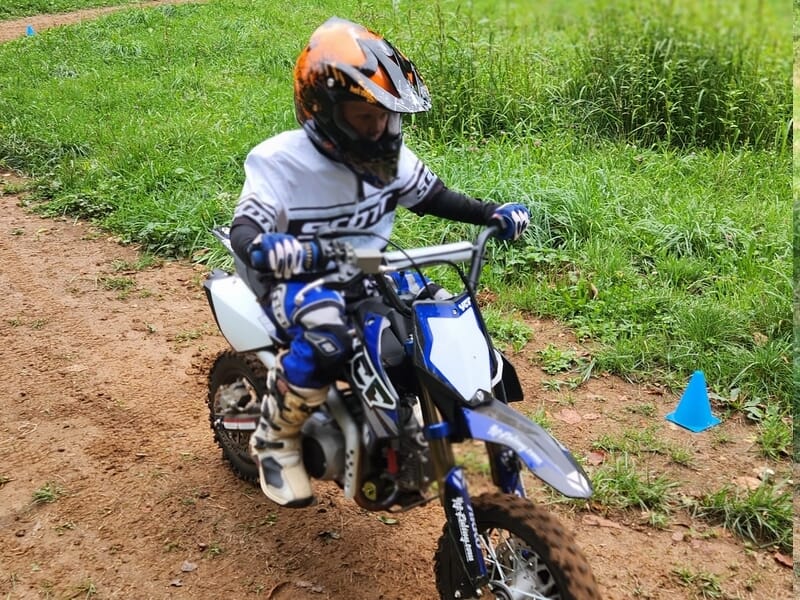 Jeune pilote en casque orange et tenue blanche, roulant lors d'un stage motocross enfant près de Lons-le-Saunier.