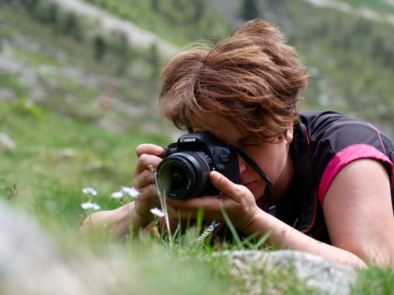 Femme allongée dans l’herbe photographiant des fleurs sauvages avec un reflex Canon en montagne.