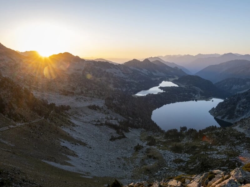 Soleil se levant derrière les crêtes, illuminant deux lacs de montagne dans une vallée rocheuse