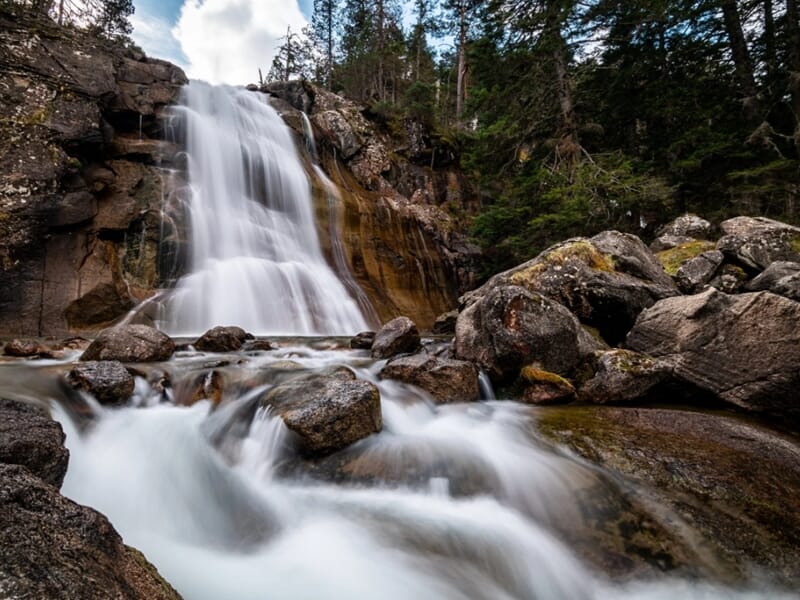 Cascade en forêt photographiée en pose longue, avec des rochers au premier plan