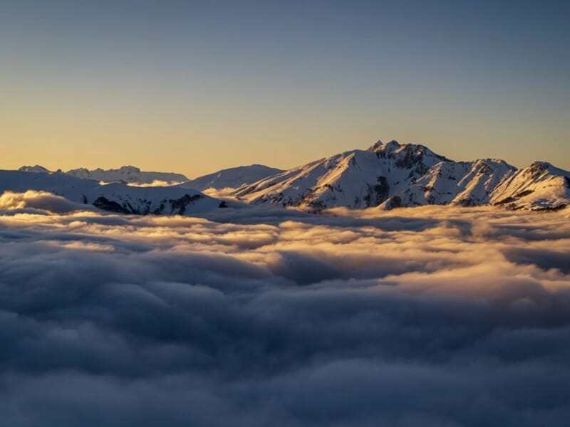 Lever du soleil illuminant une mer de nuages et des sommets enneigés