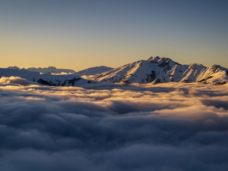 Lever du soleil illuminant une mer de nuages et des sommets enneigés