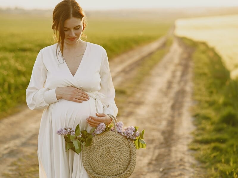 femme enceinte dans un champ au coucher de soleil, panier fleuri.