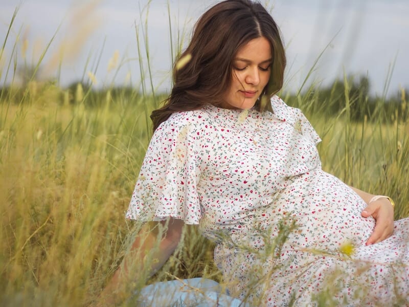 femme enceinte dans un champ, robe fleurie, regard tendre.