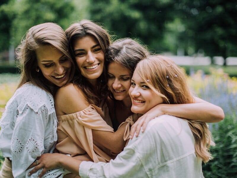 Quatre jeunes femmes souriantes se prennent dans les bras dans un parc fleuri