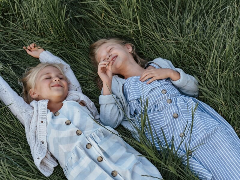 Deux fillettes rient allongées dans l’herbe haute, moment de jeu et de bonheur en plein air.