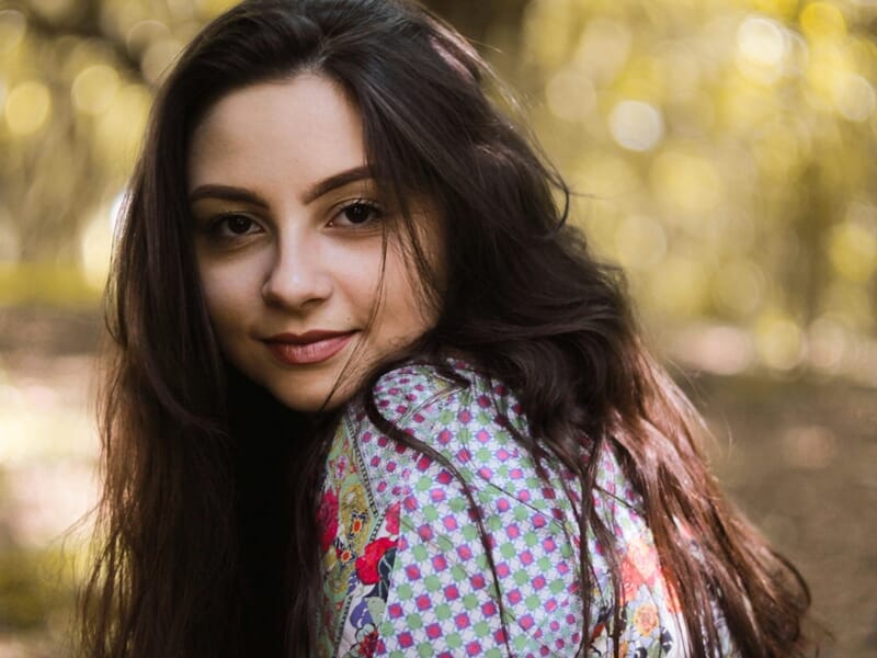 Portrait d’une femme au regard doux, vêtue d’une chemise colorée, en extérieur dans une lumière dorée.