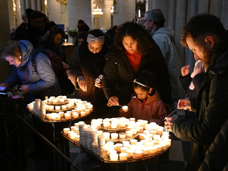 Personnes allumant des bougies votives dans une cathédrale, moment de recueillement collectif.