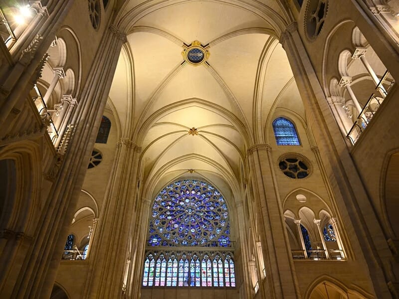 Nef d’une cathédrale illuminée, avec voûtes en ogive et grande rosace en vitrail au fond.