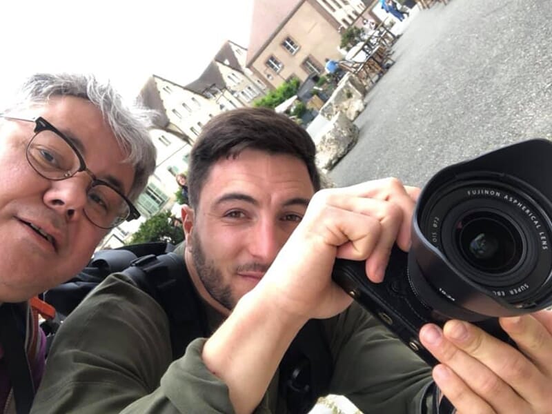 Deux hommes prennent un selfie pendant qu’un d’eux tient un appareil photo Fujifilm.