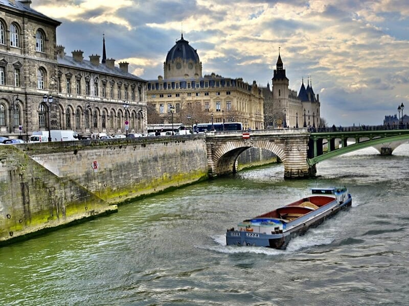 Péniche naviguant sur la Seine, avec vue sur la Conciergerie et un pont parisien.