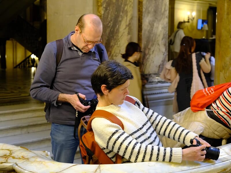 Deux personnes consultent leurs appareils photo à l’intérieur d’un bâtiment au décor en marbre.