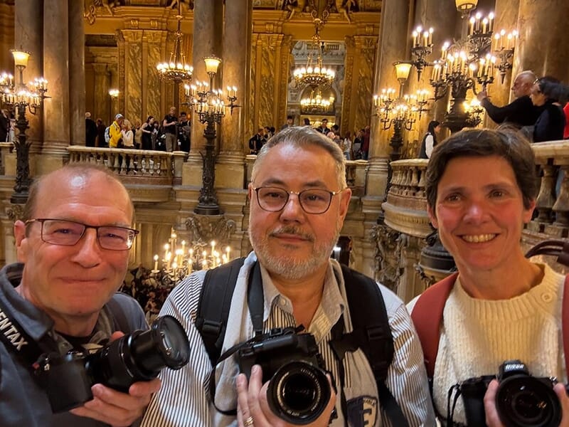 Trois personnes posent avec leurs appareils photo dans un lieu richement décoré et éclairé.