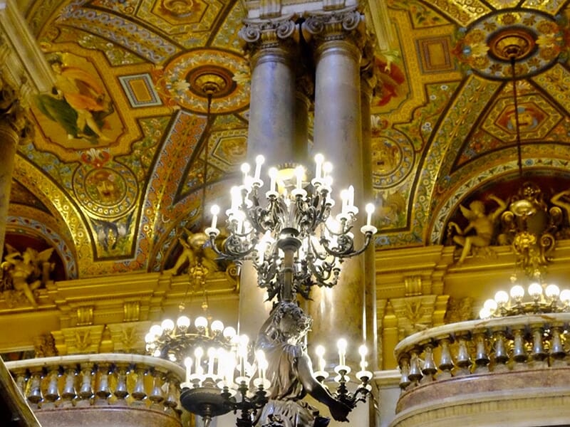 Détail d’un lustre allumé et d’un plafond richement décoré dans un bâtiment historique.