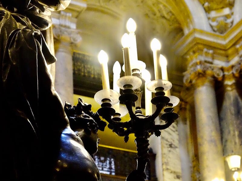 Vue rapprochée d’un chandelier allumé, silhouette d’une statue en contre-jour.