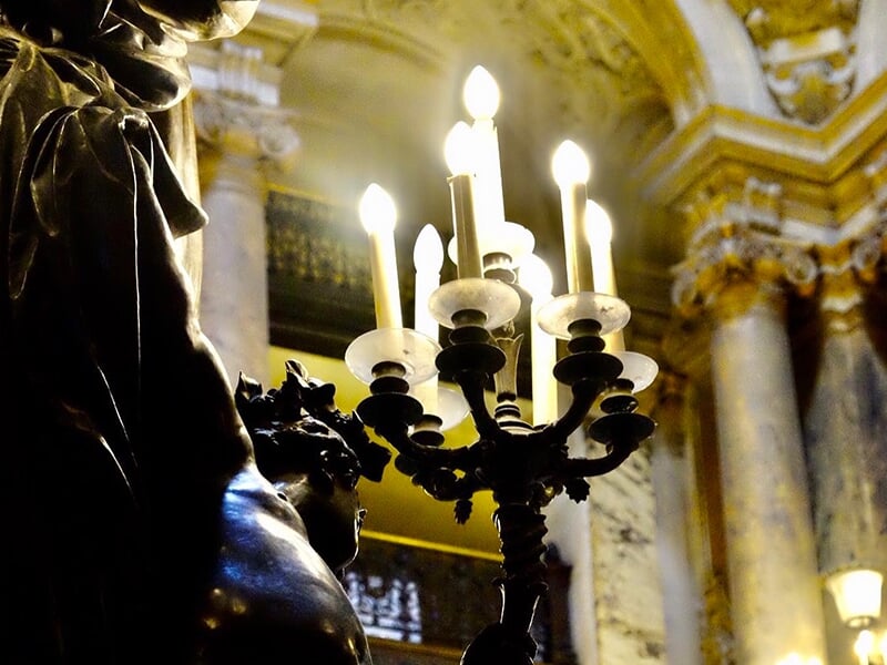 Vue rapprochée d’un chandelier allumé, silhouette d’une statue en contre-jour.