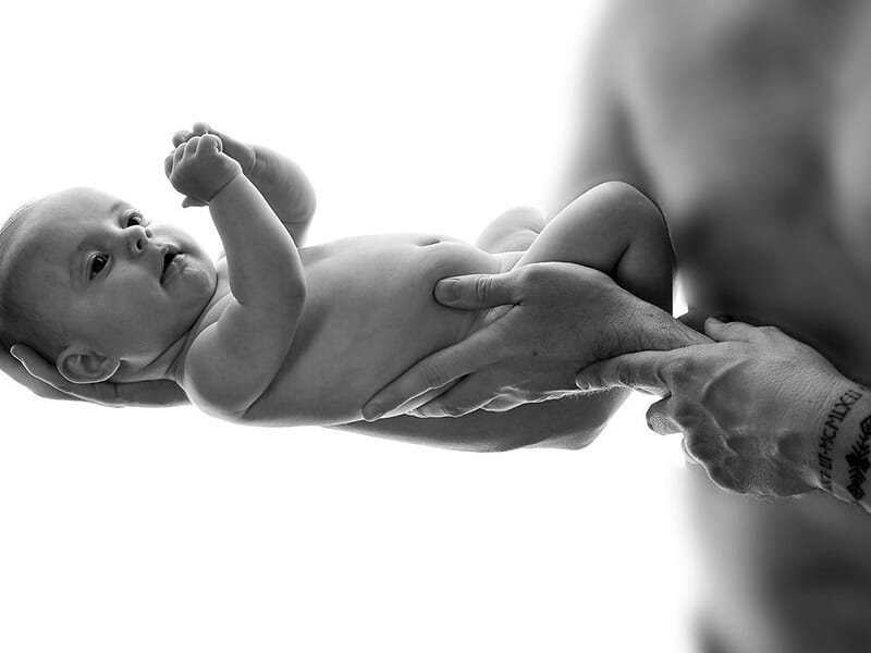 Bébé nu tenu délicatement par un adulte, en noir et blanc.