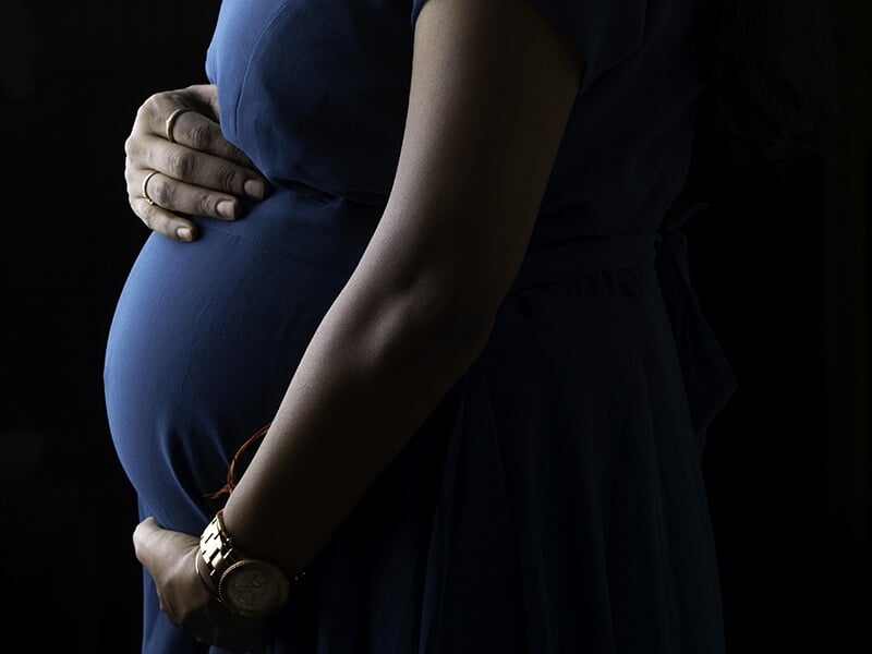 Femme enceinte en robe bleue, dans une ambiance sombre, tenant son ventre avec les deux mains.