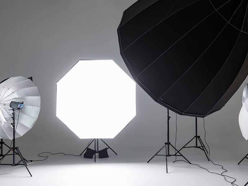 Équipements de studio photo avec plusieurs diffuseurs de lumière, softbox et parapluies installés dans un espace blanc.