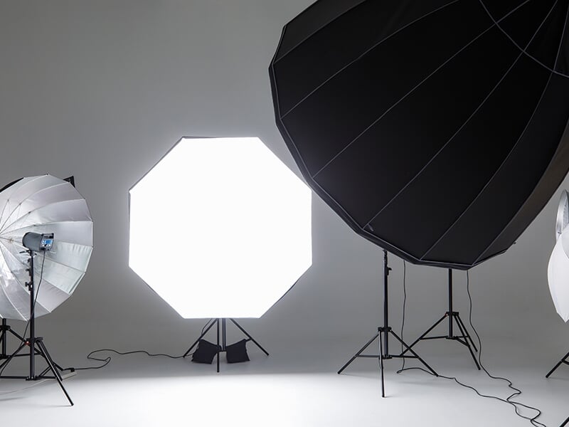 Équipements de studio photo avec plusieurs diffuseurs de lumière, softbox et parapluies installés dans un espace blanc.