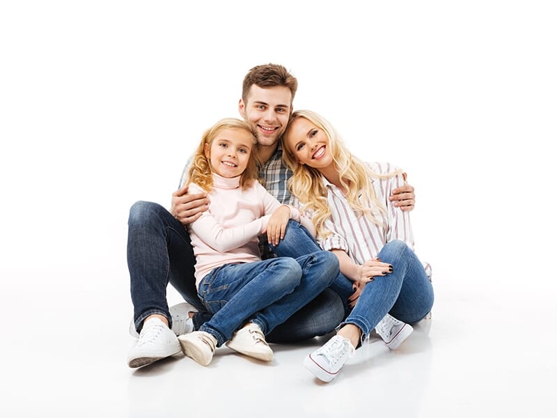 Famille souriante posant dans un studio photo sur fond blanc, composée d’un père, d’une mère et de leur fille.