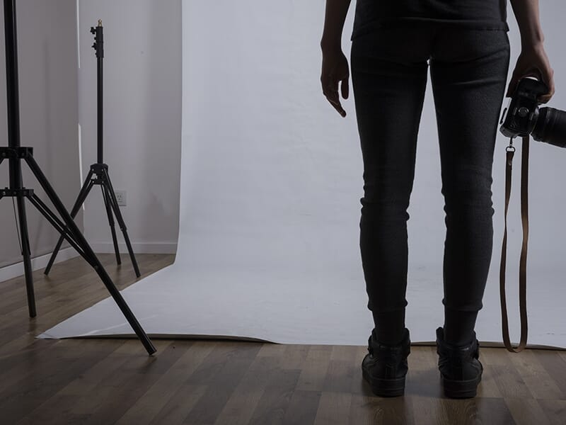 Personne debout devant un fond de studio blanc, appareil photo à la main, vue de dos.