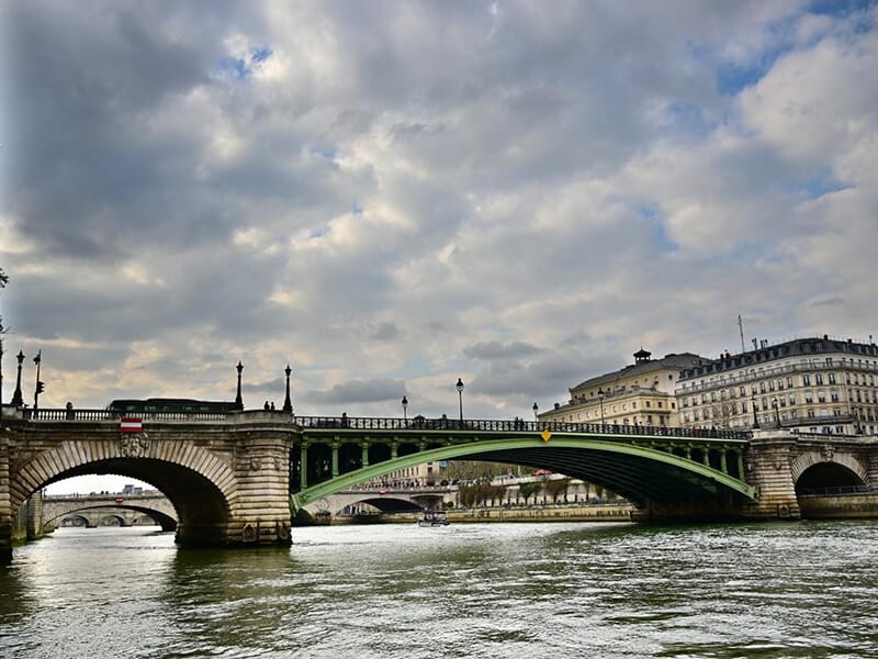 Pont sur la Seine à Paris, avec circulation de voitures et piétons, sous un ciel nuageux en fin de journée.