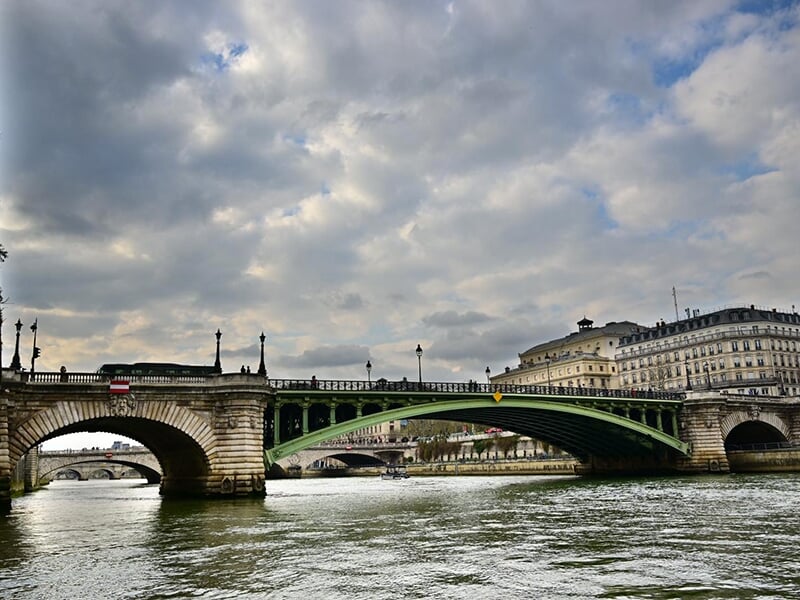 Pont sur la Seine à Paris, avec circulation de voitures et piétons, sous un ciel nuageux en fin de journée.