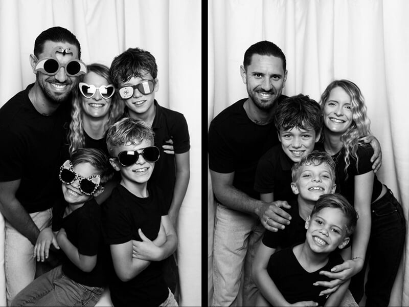 Photo en noir et blanc d'une famille souriante avec des lunettes amusantes posant devant un rideau blanc.