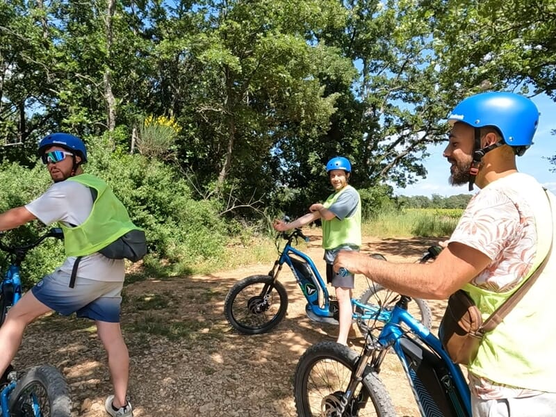 Trois hommes avec casque bleu et gilet de sécurité en pleine sortie en trottinette électrique tout-terrain.