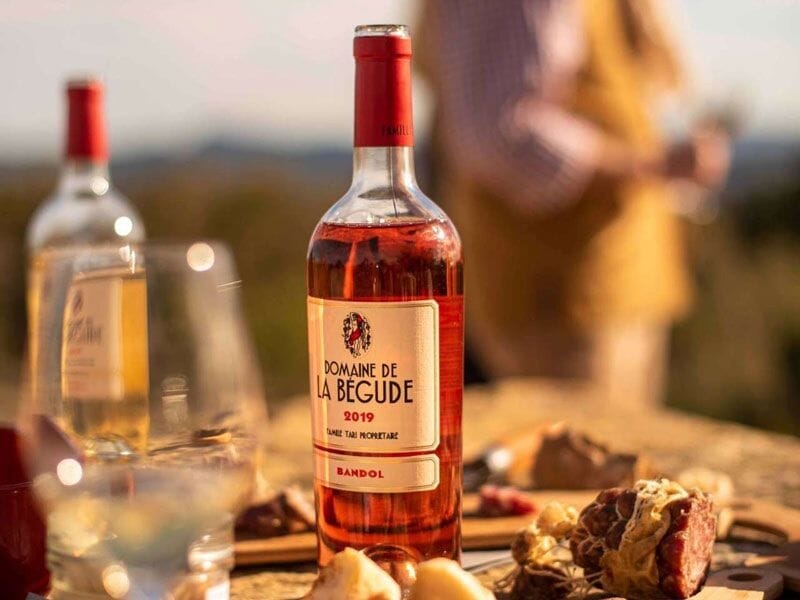 Bouteille de vin rosé Domaine de la Bégude 2019 posée sur une table en bois avec verres et charcuterie en arrière-plan.