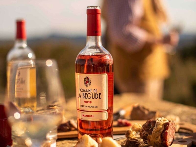Bouteille de vin rosé Domaine de la Bégude 2019 posée sur une table en bois avec verres et charcuterie en arrière-plan.