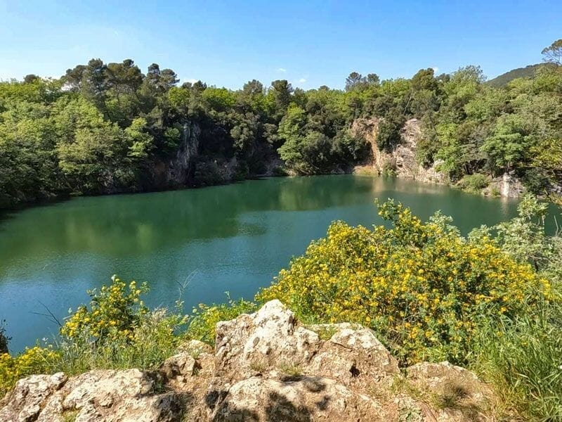 Vue d'un lac entouré de rochers et de végétation dense sous un ciel clair, paysage naturel paisible.