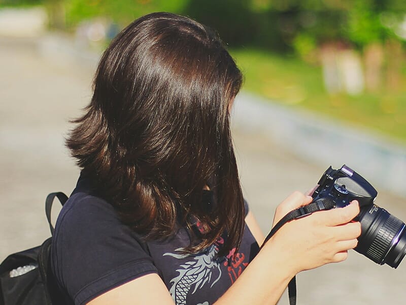 Jeune femme consultant son appareil photo en plein air, dos partiellement tourné.