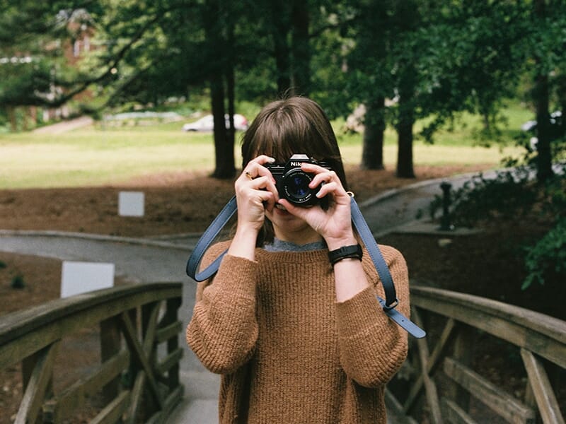 Jeune femme consultant son appareil photo en extérieur, en pleine lumière naturelle.