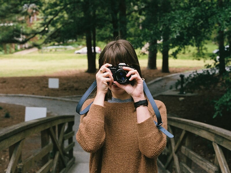 Jeune femme consultant son appareil photo en extérieur, en pleine lumière naturelle.