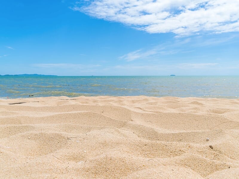 Plage de sable fin sous un ciel bleu, avec l’horizon marin au loin.