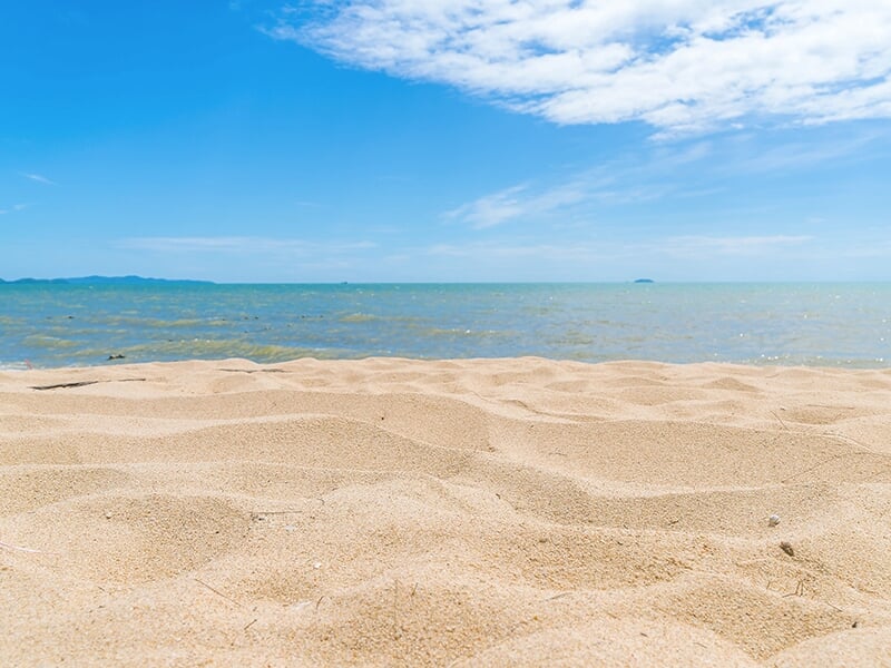 Plage de sable fin sous un ciel bleu, avec l’horizon marin au loin.