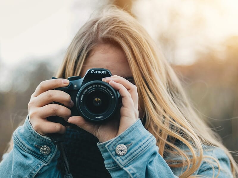 Jeune femme blonde tenant un appareil photo Canon en position de prise de vue.
