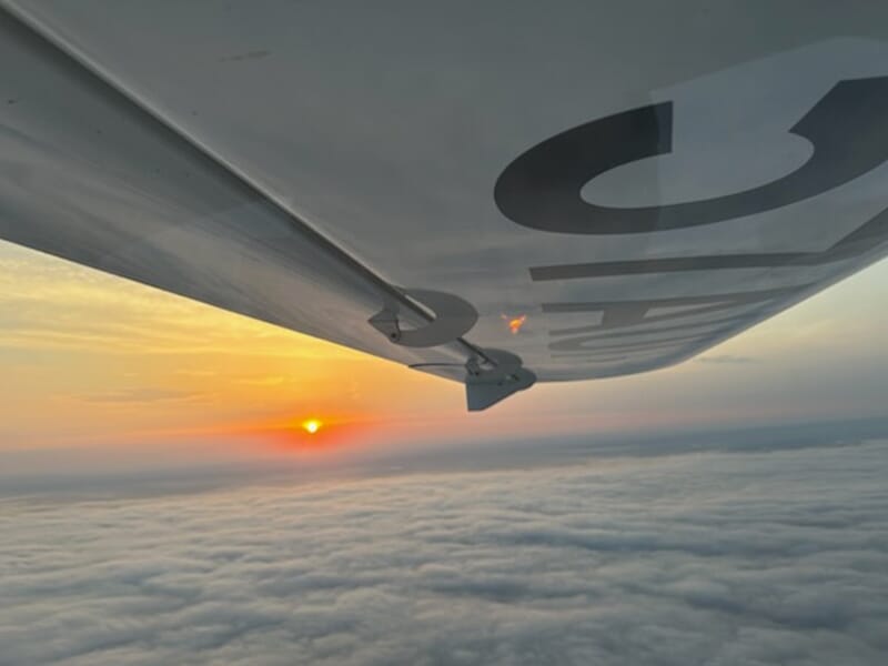 Vue aérienne d’un coucher de soleil au-dessus des nuages prise depuis l’aile d’un avion léger.