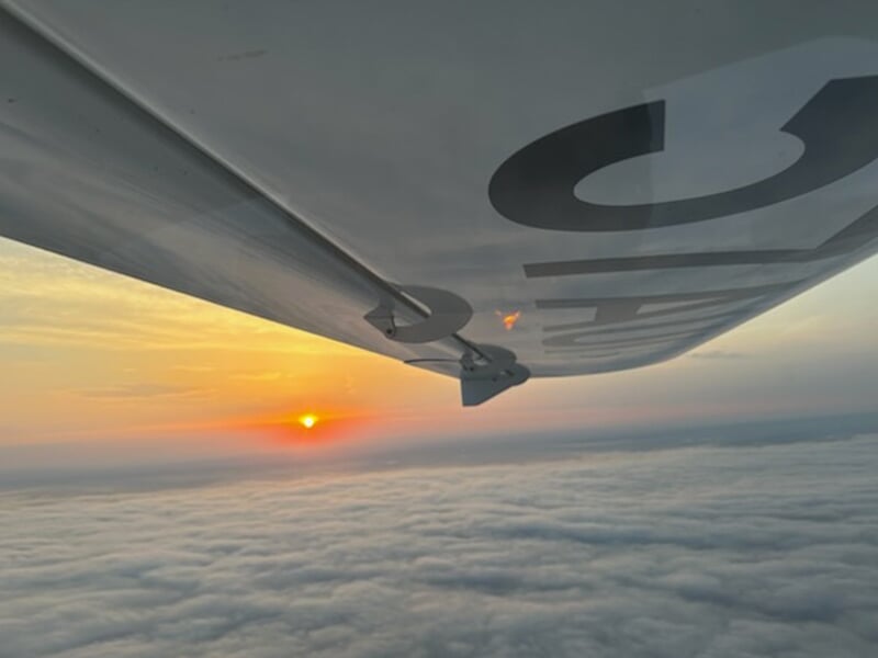Vue aérienne d’un coucher de soleil au-dessus des nuages prise depuis l’aile d’un avion léger.