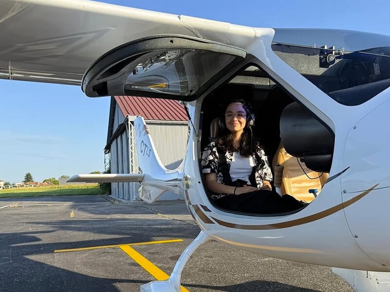 Femme souriante assise dans un avion léger CTLS, casque sur les oreilles, prête à décoller.