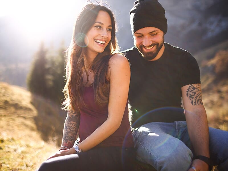 Couple souriant assis en montagne, complices et enjoués sous une lumière dorée de fin de journée.