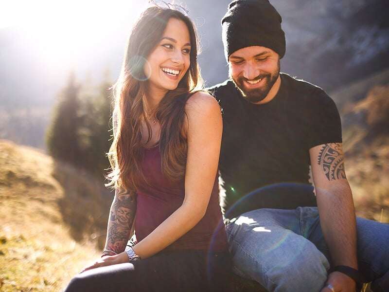Couple souriant assis en montagne, complices et enjoués sous une lumière dorée de fin de journée.