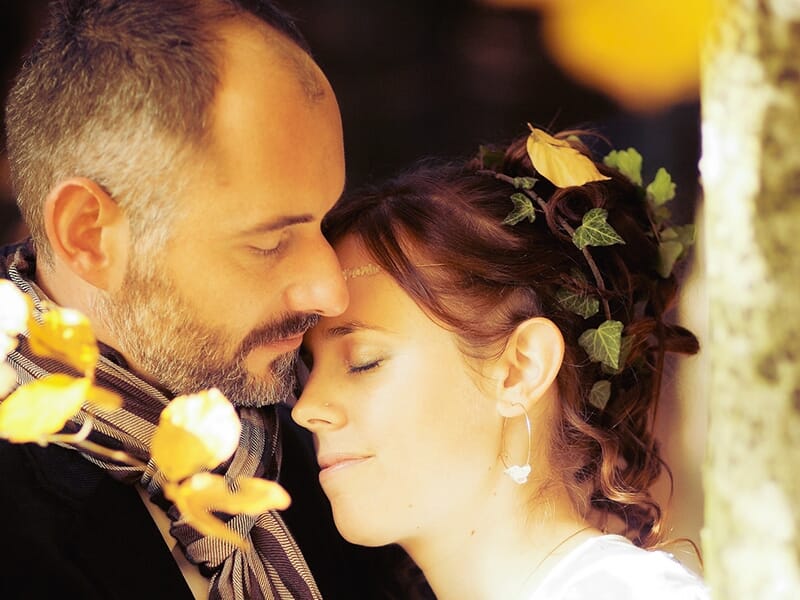 Couple enlacé dans un décor automnal, la femme les yeux fermés appuyée contre l’homme dans une ambiance douce et chaleureuse.
