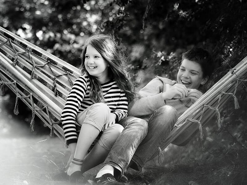 Deux enfants riant ensemble dans un hamac, en noir et blanc, scène joyeuse et complice.