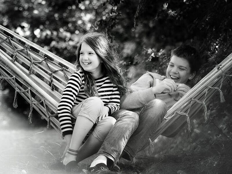 Deux enfants riant ensemble dans un hamac, en noir et blanc, scène joyeuse et complice.
